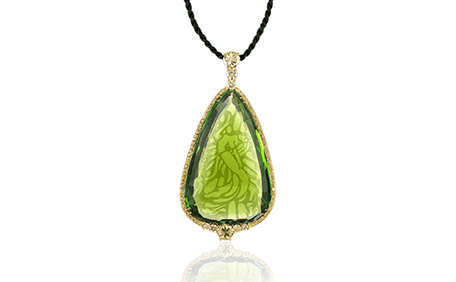 Pear-shaped peridot pendant with intricate patterns, set in a gold frame and suspended from a black cord.