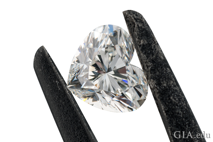 A heart shaped diamond held in a pair of jeweler’s tweezers.