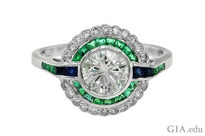 A 1.09 carat round brilliant cut diamond engagement ring from the Art Deco era, featuring emeralds, sapphires set in 18K white gold.