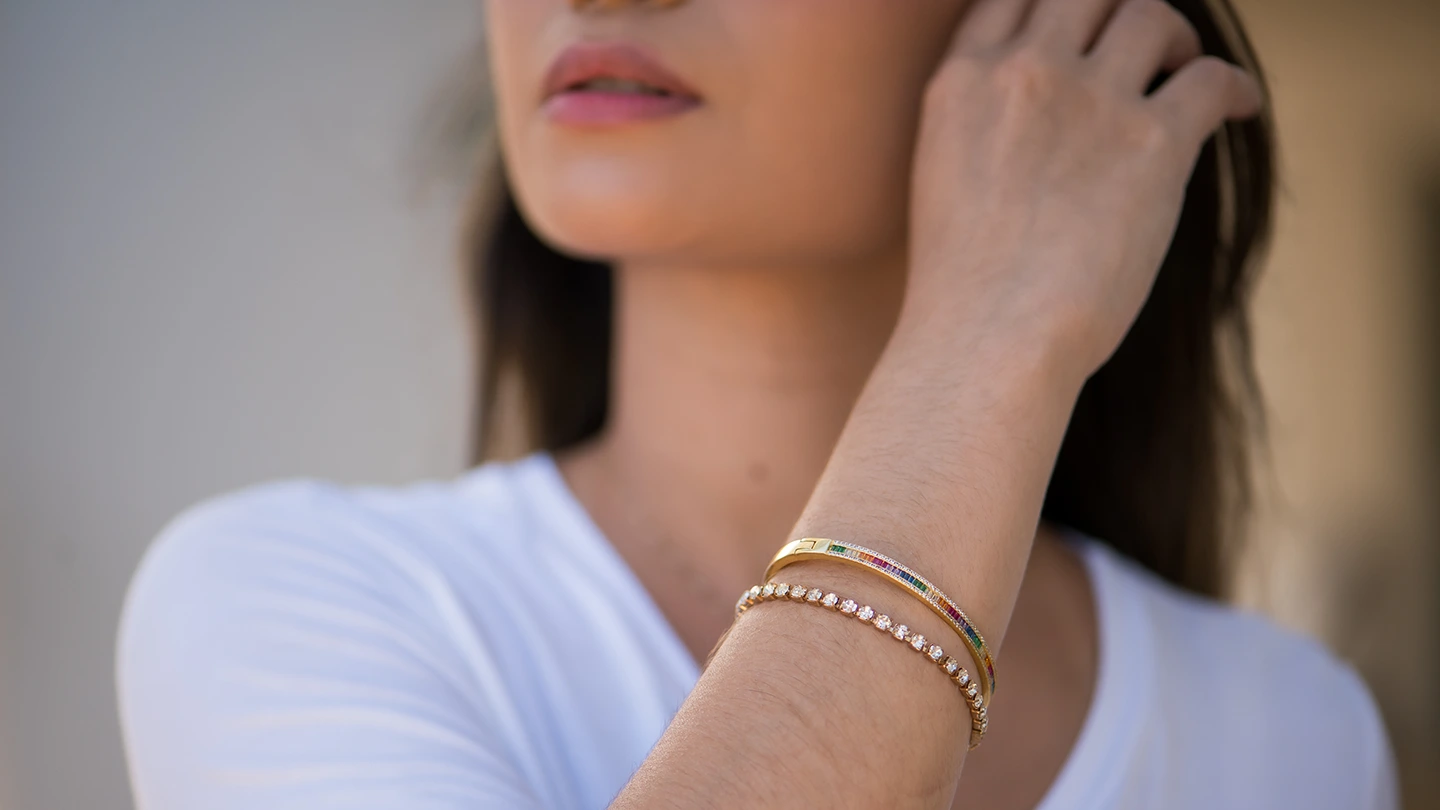 Close-up of a diamond rose gold tennis bracelet and rainbow bangle bracelet stacked on a woman's wrist.