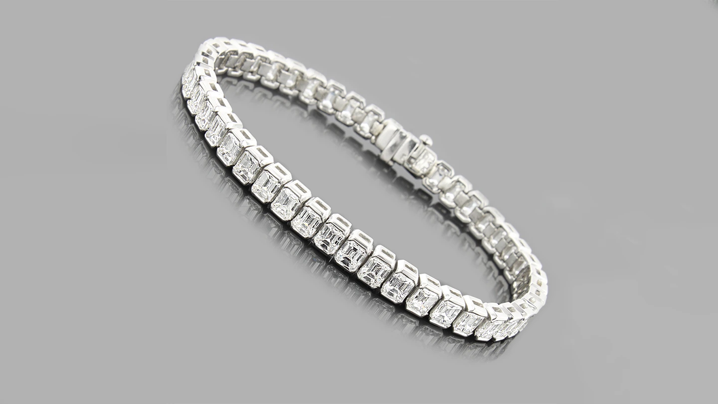Emerald cut diamond tennis bracelet against gray background.