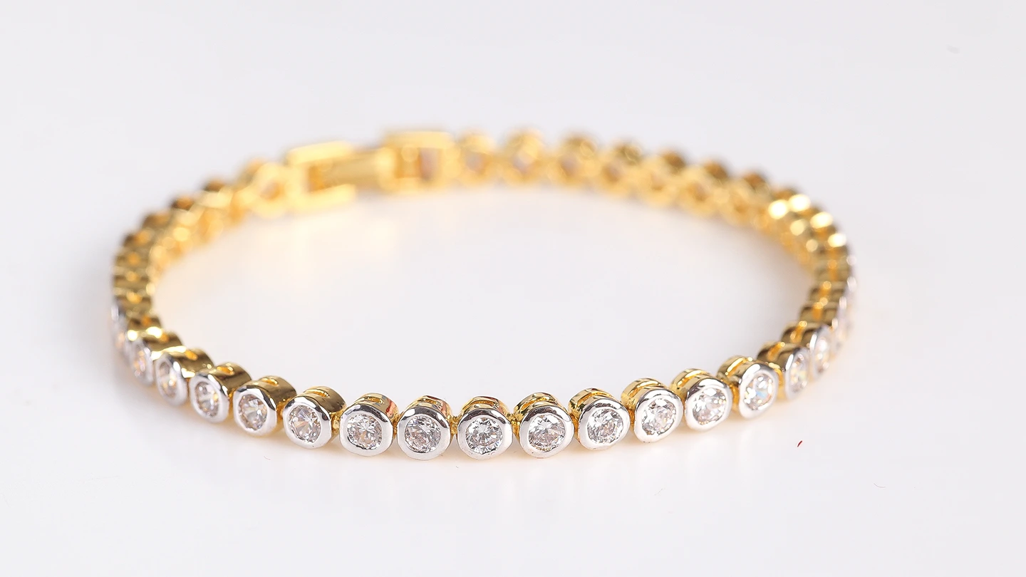 A white and yellow gold diamond tennis bracelet against a gray background.