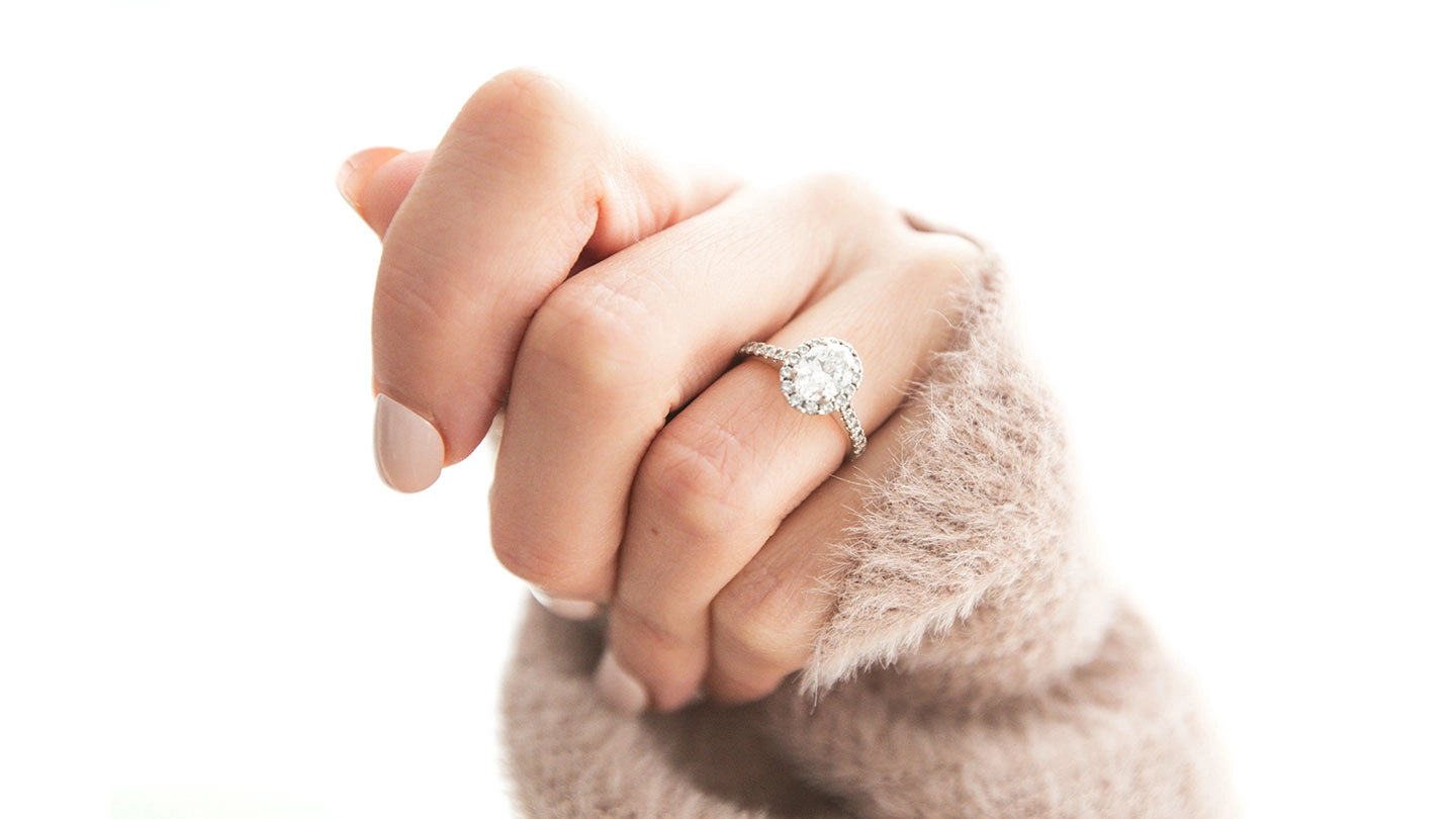 Woman’s hand with oval diamond engagement ring on white background.