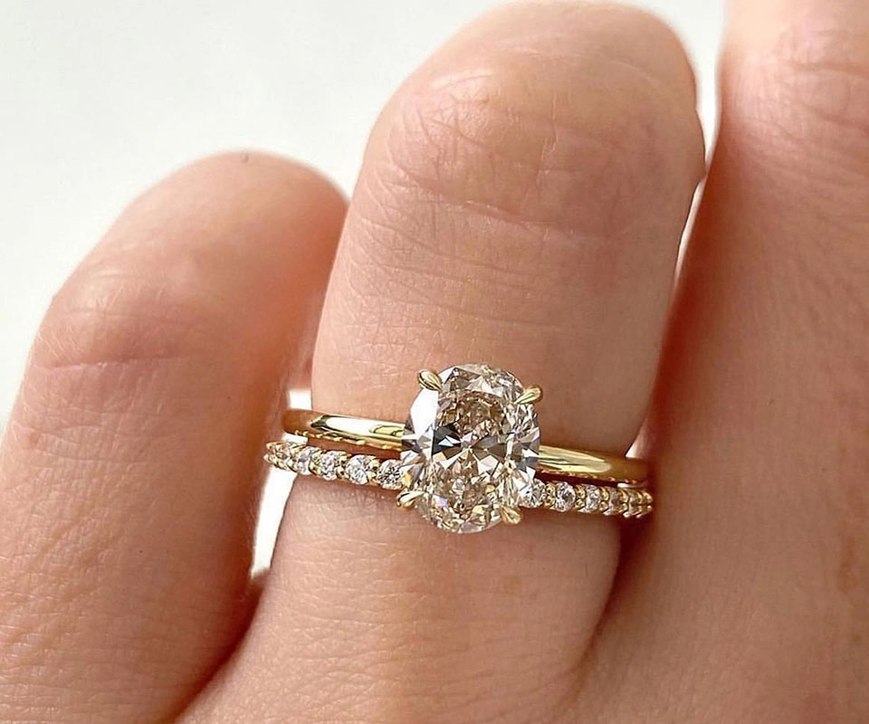Oval solitaire diamond engagement ring with pavé wedding band on ring finger against white background