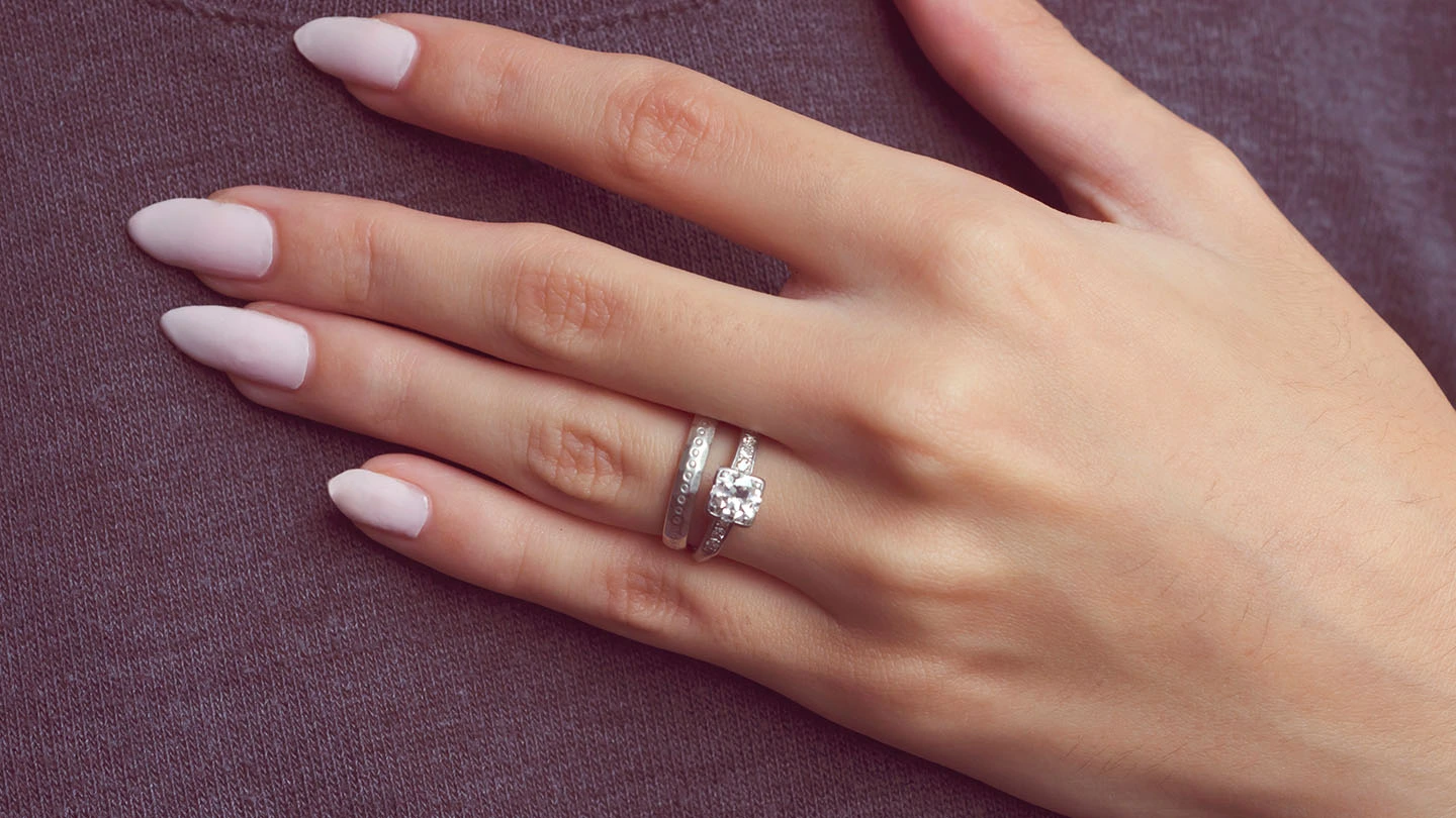 Woman’s hand showing a wedding band stacked top of a diamond engagement ring.