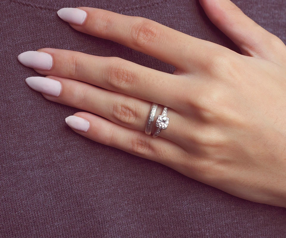 Woman’s hand showing a wedding band stacked top of a diamond engagement ring