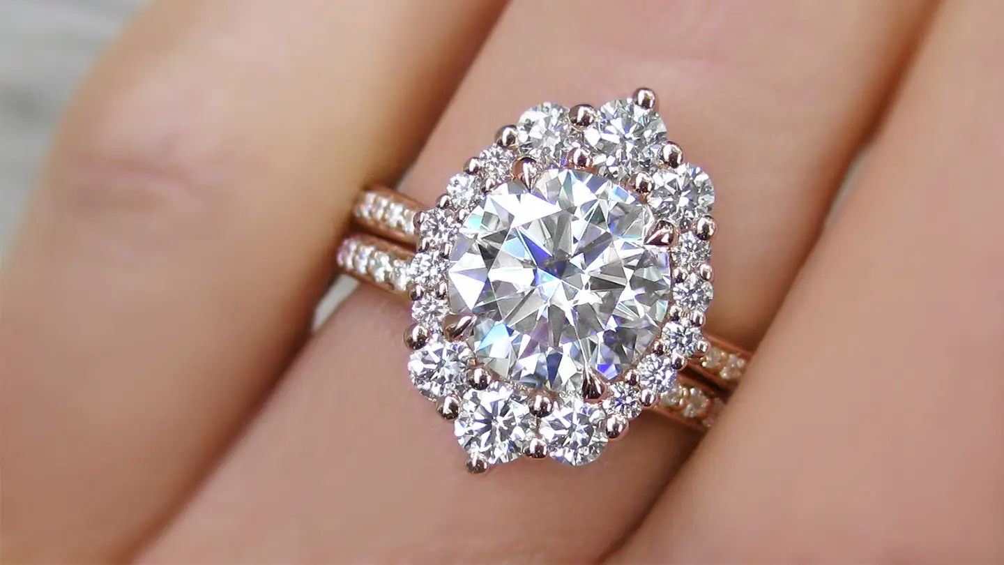 Closeup of a moissanite engagement ring set in rose gold with diamond halo on woman’s hand