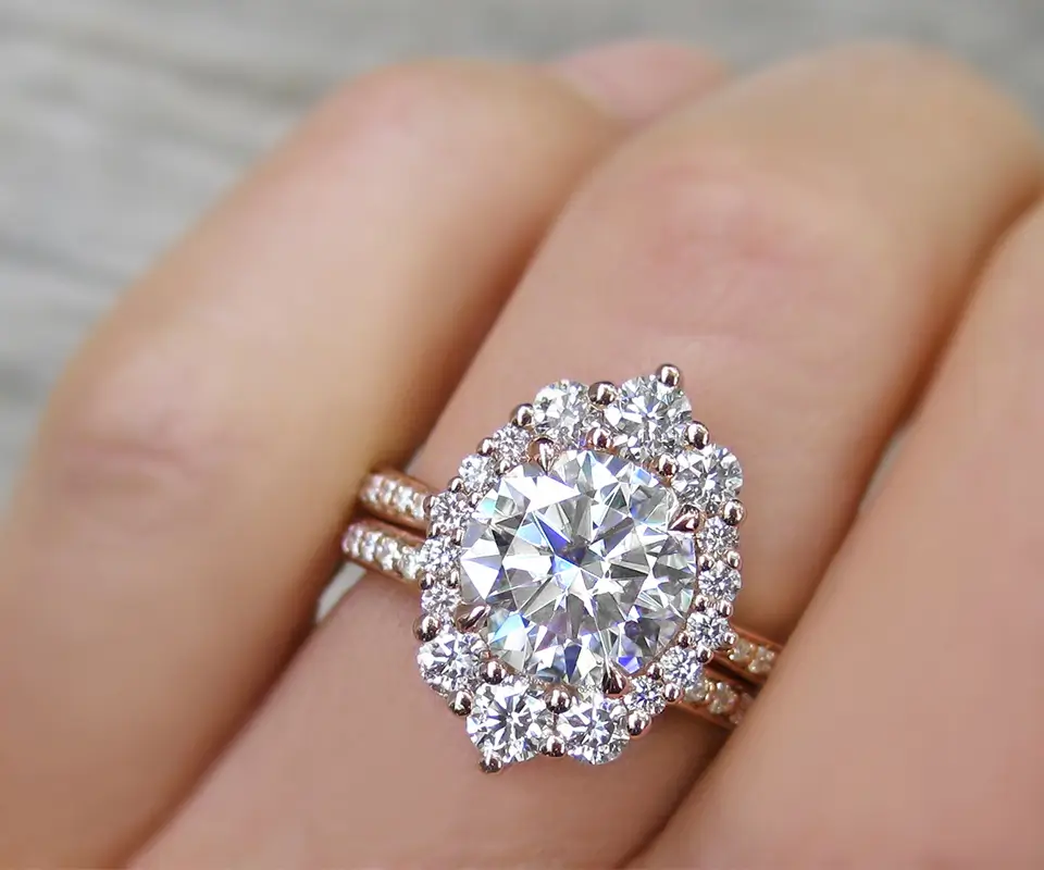Closeup of a moissanite engagement ring set in rose gold with diamond halo on woman’s hand