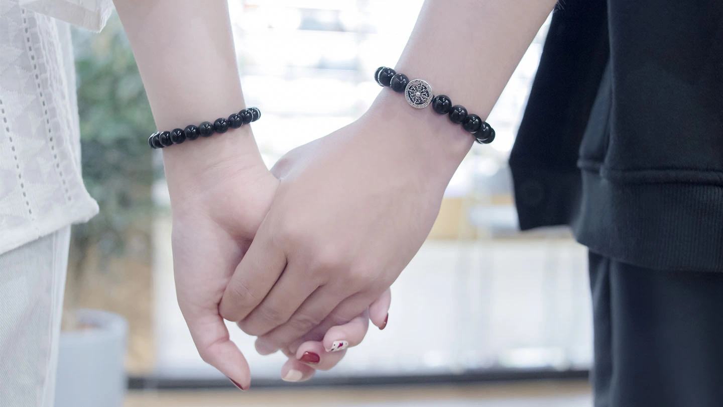 Close-up of two people holding hands wearing matching bracelets.