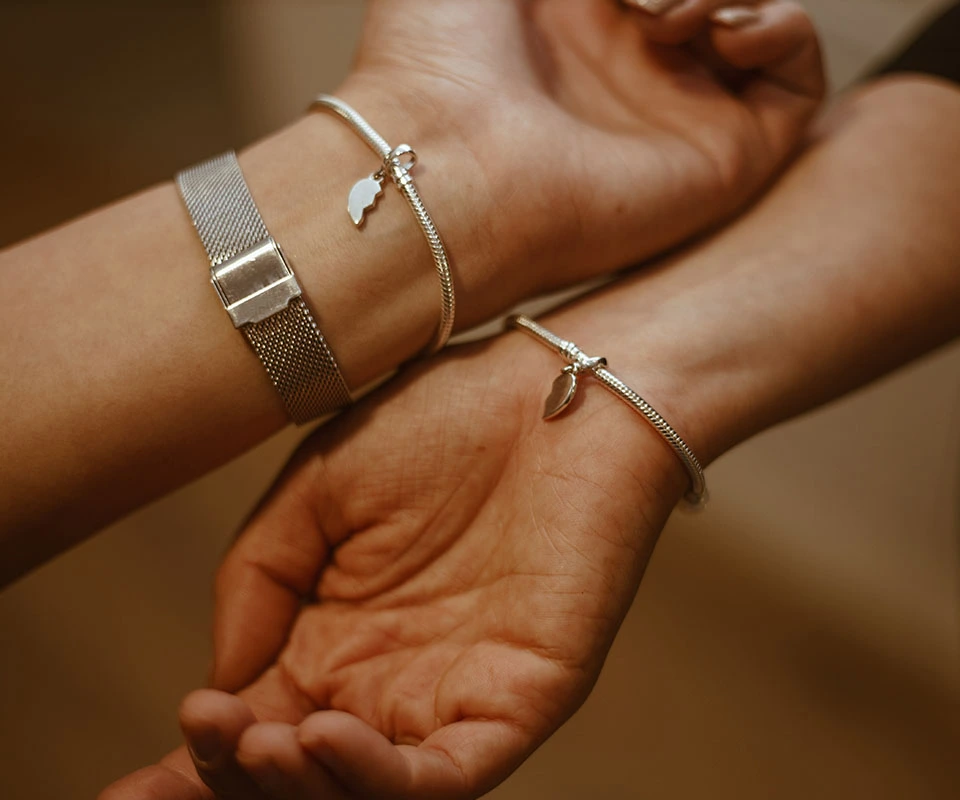 Close-up of two people’s hands wearing matching bracelets with split heart charms