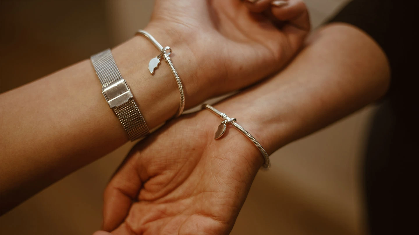 Close-up of two people’s hands wearing matching bracelets with split heart charms.