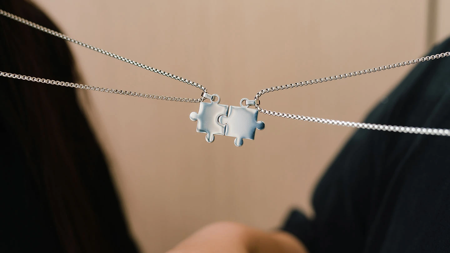 Two puzzle piece charm necklaces interlocked together.
