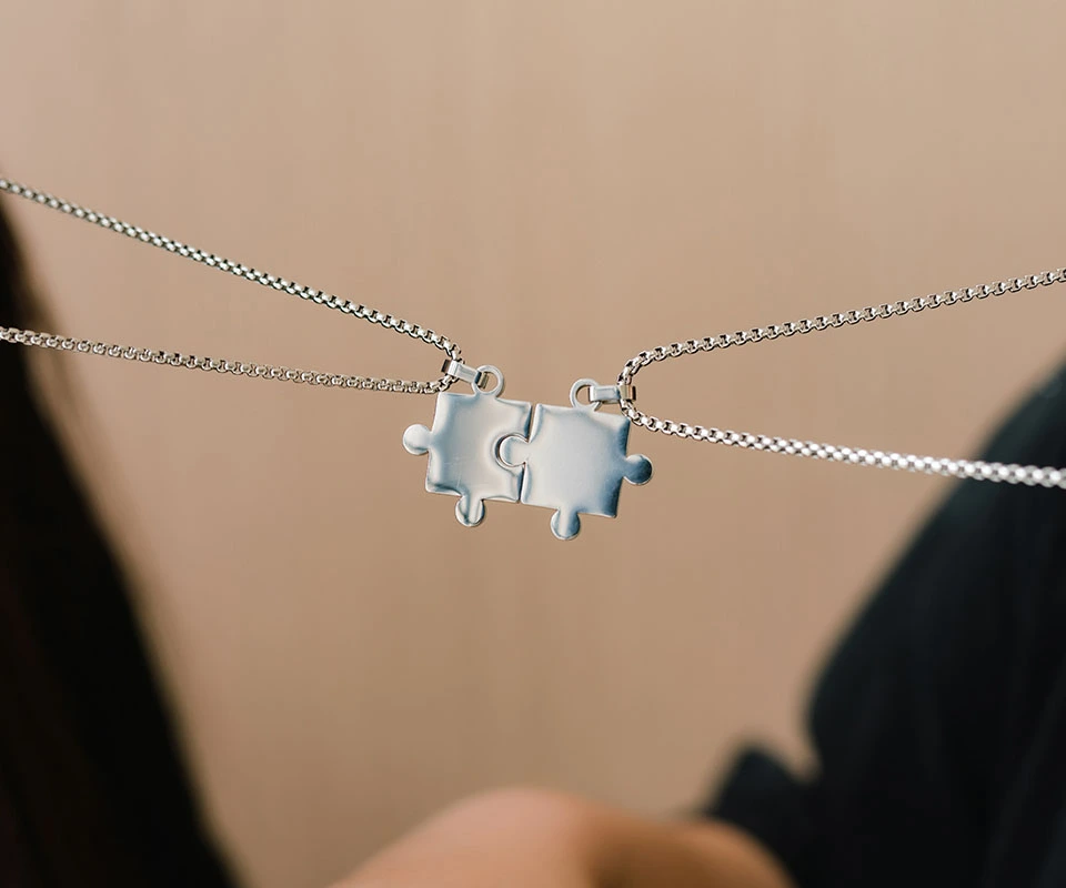 Two puzzle piece charm necklaces interlocked together