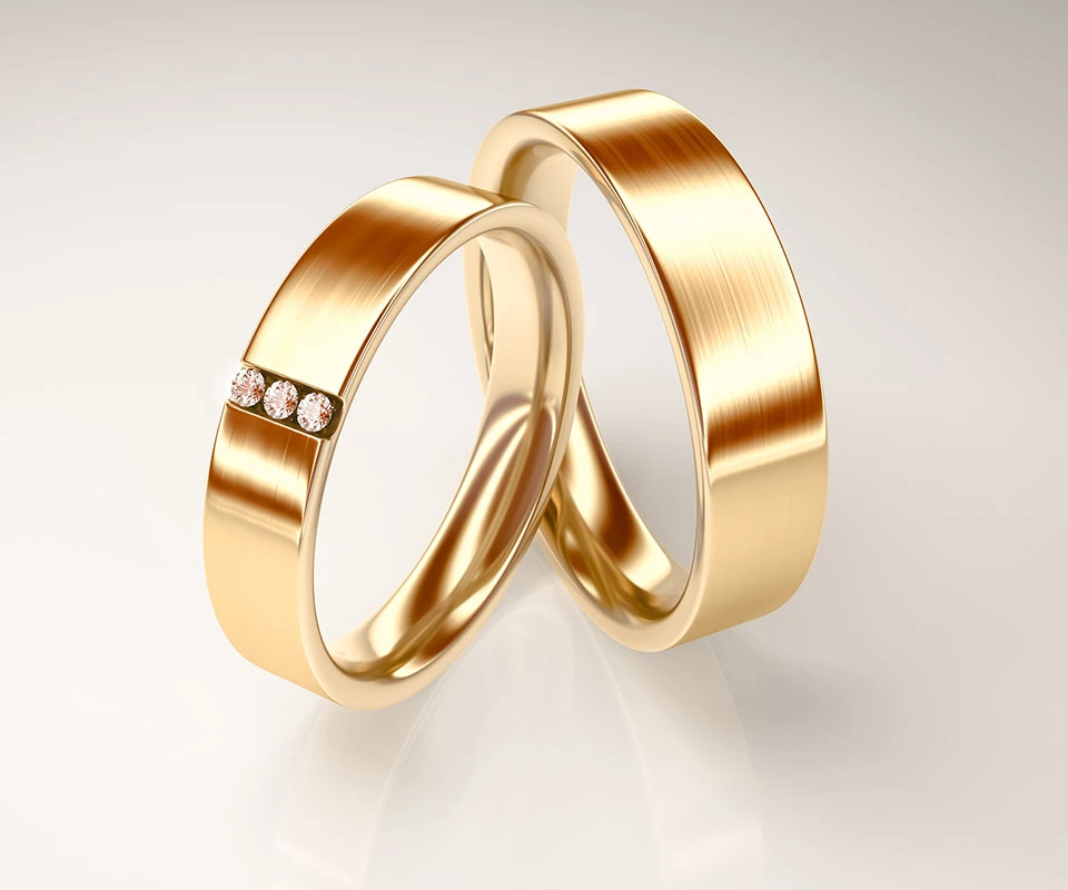 A set of gold cigar wedding bands with tension-set diamonds on a gray background