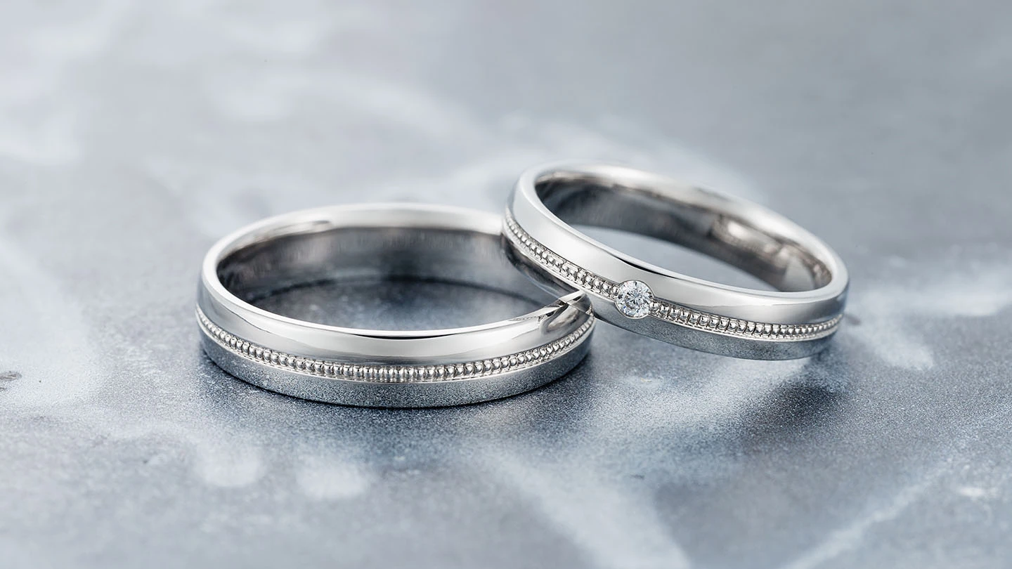 Matching white gold wedding bands with milgrain on a gray table.