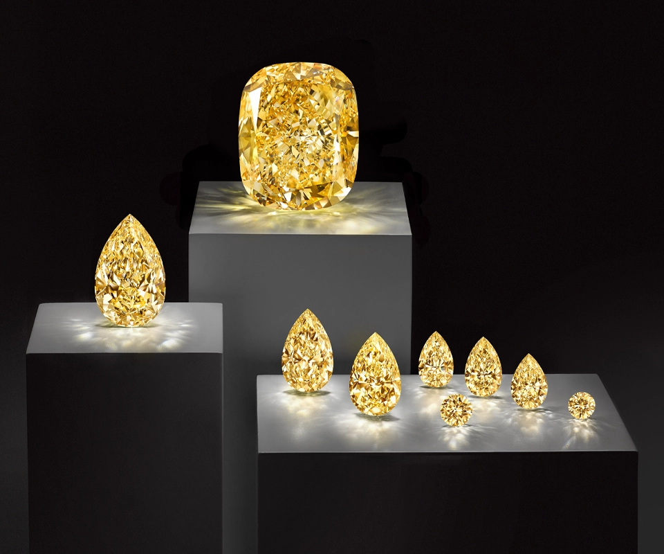Fancy Intense Yellow Graff Empress diamond with smaller yellow diamonds from the same crystal, displayed on podiums against a black background