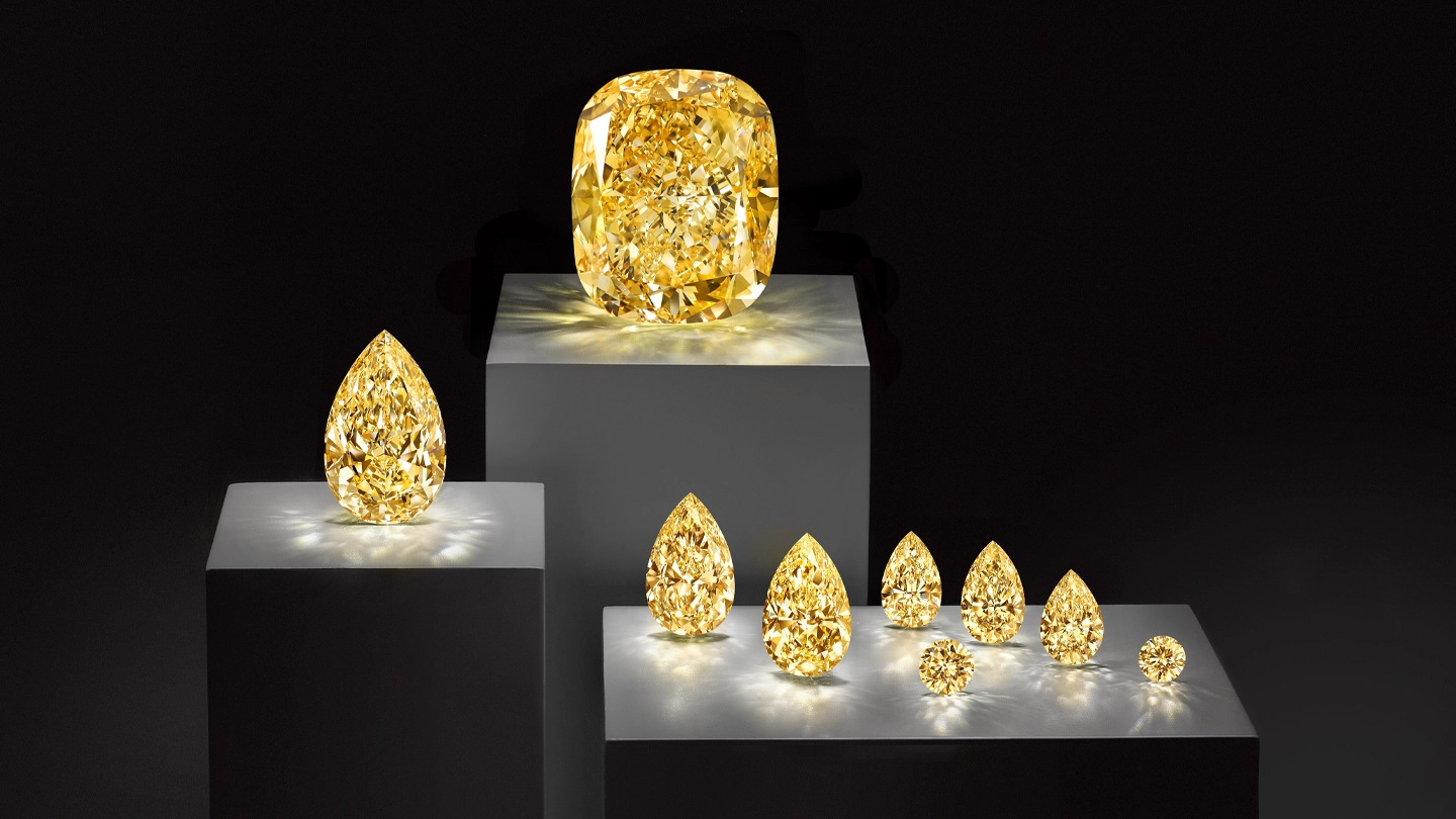Fancy Intense Yellow Graff Empress diamond with smaller yellow diamonds from the same crystal, displayed on podiums against a black background