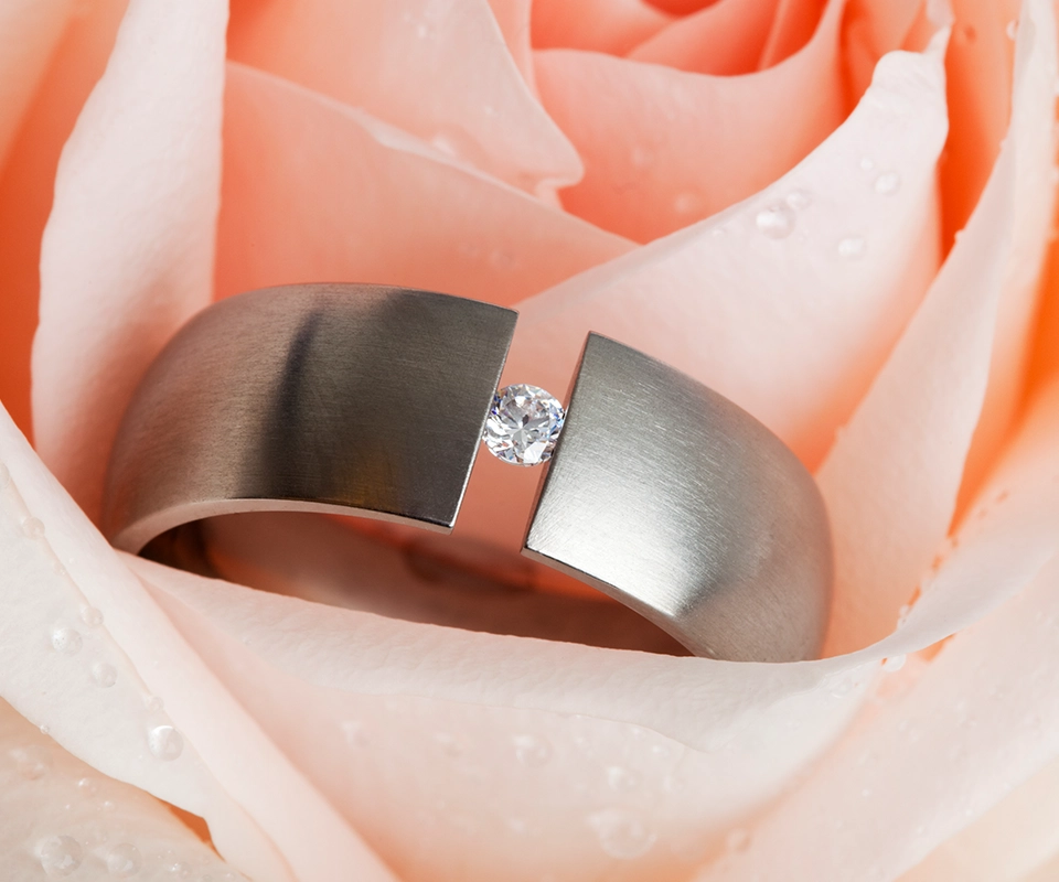 Diamond tension-set ring with floating round brilliant center stone nestled in the petals of a dewy, pink rose