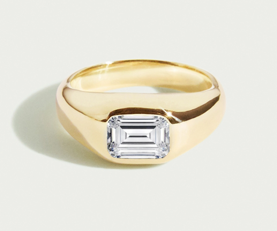 Flush-set emerald-cut diamond in wide yellow gold ring.